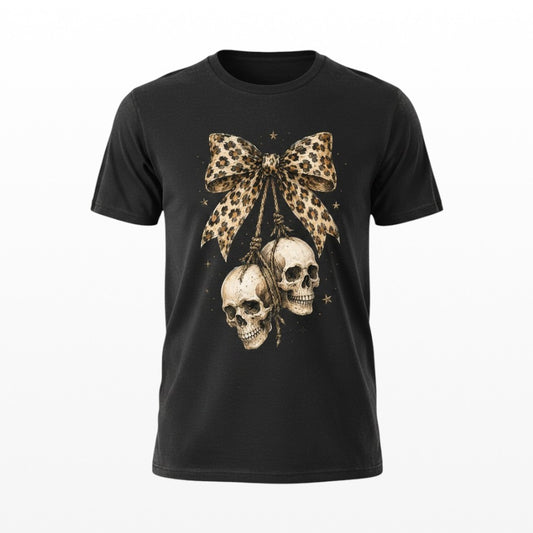A black short-sleeve crewneck t-shirt featuring a graphic print of two hanging skulls suspended from a leopard-print bow, with small gold stars around them, shown against a plain white background.