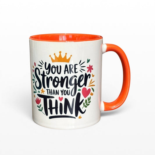Illustrated Solutions Store white ceramic mug with orange handle and interior, featuring the quote "You are stronger than you think" with floral and crown graphics.