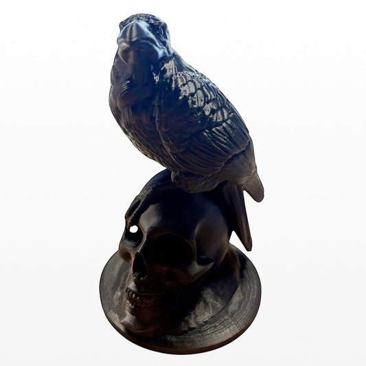 Illustrated Solutions Store matte black raven figurine perched on a skull base, gothic décor.