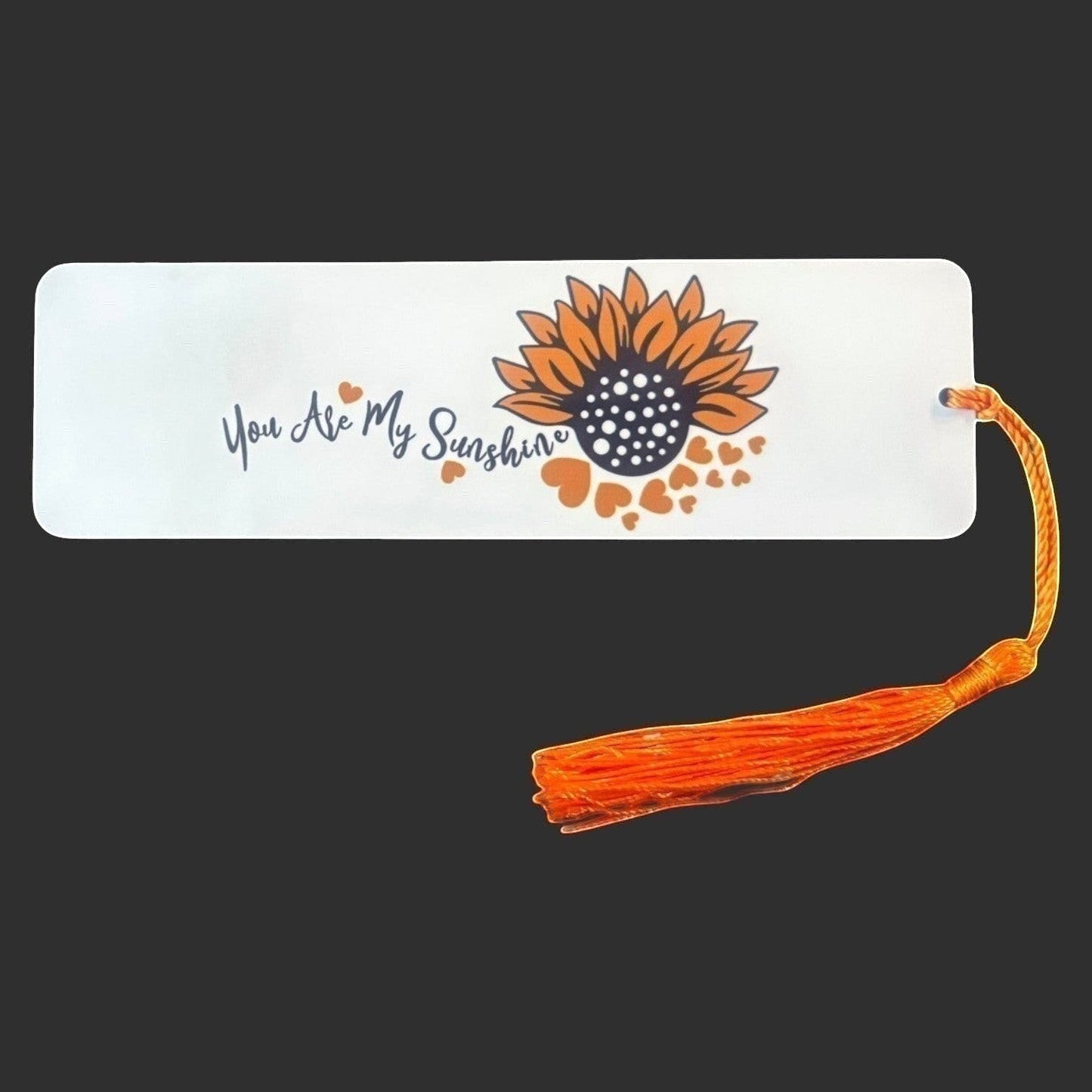 Illustrated Solutions Store metal bookmark featuring a sunflower and the text You Are My Sunshine with an orange tassel. Large view on dark background.