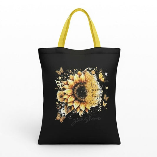 Illustrated Solutions Store yellow handle black tote bag with yellow handles, featuring a large sunflower design with butterflies and leopard print accents. Text reads 'When you can't find the sunshine, be the sunshine.'
