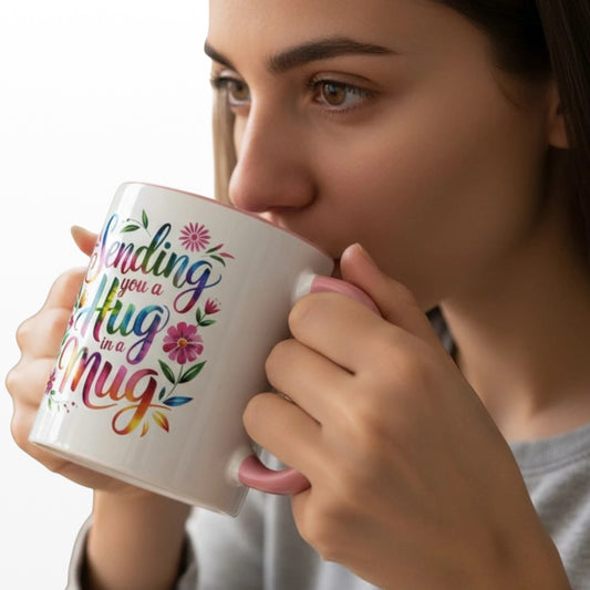 Woman drinking from a white ceramic mug with a pink handle and interior, featuring colourful "Sending you a Hug in a Mug" text and floral accents.