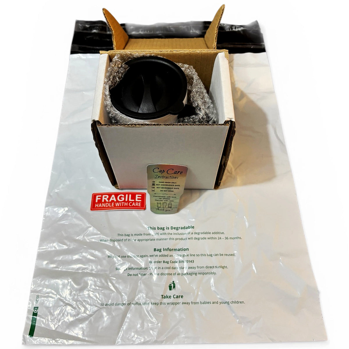 Protective box for travel mug, showing packaging, care label, fragile sticker (in red and white) and degradable bag