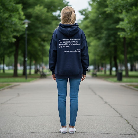 Person standing on a path in a park, wearing a navy hoodie with a white motivational quote on the back.