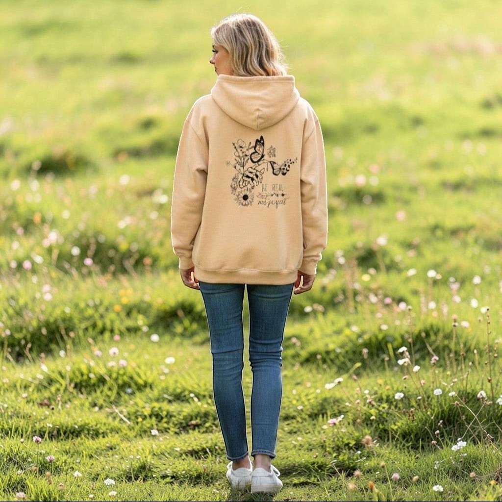 Person wearing a beige hoodie with floral designs and text, standing in a field.