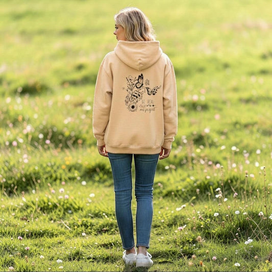Person wearing a beige hoodie with floral designs and text, standing in a field.