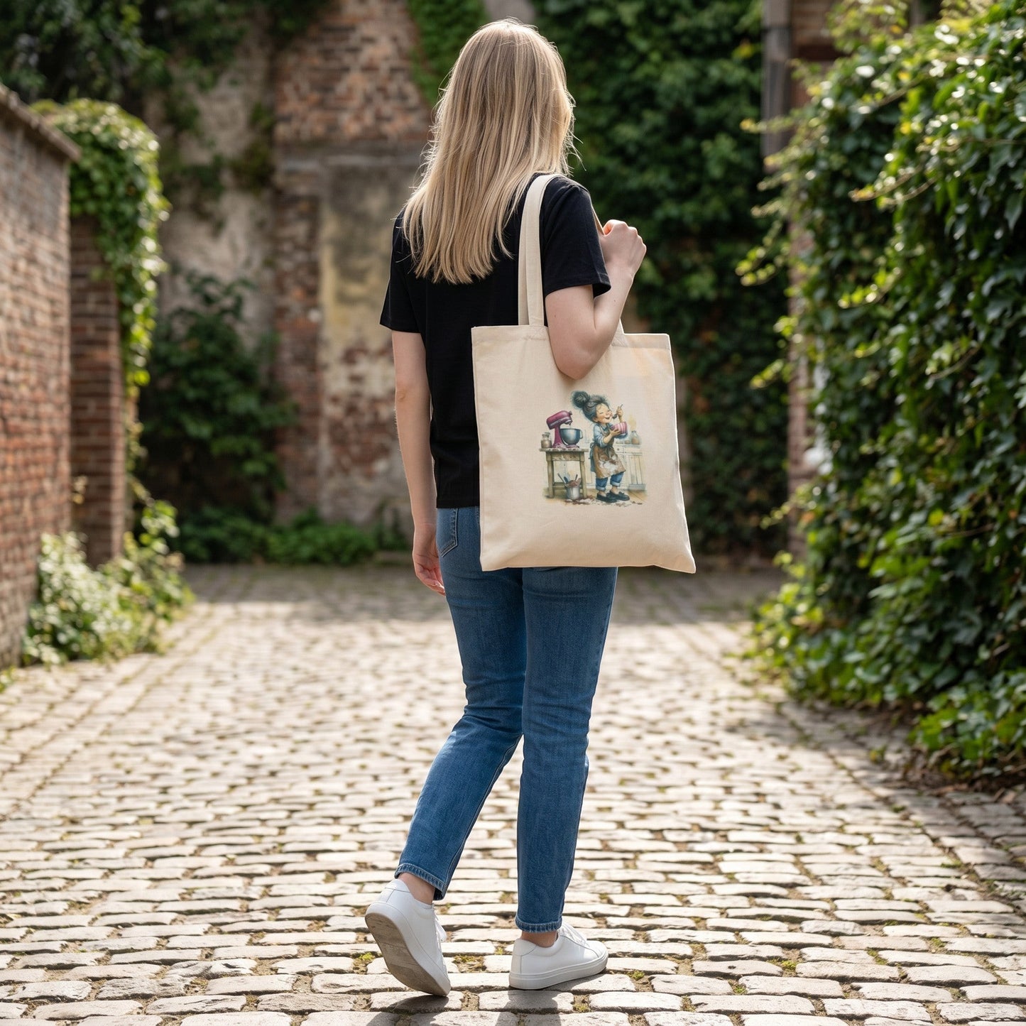 Woman carrying a beige Illustrated Solutions Store hobby tote bag with a baking character design on a cobblestone path