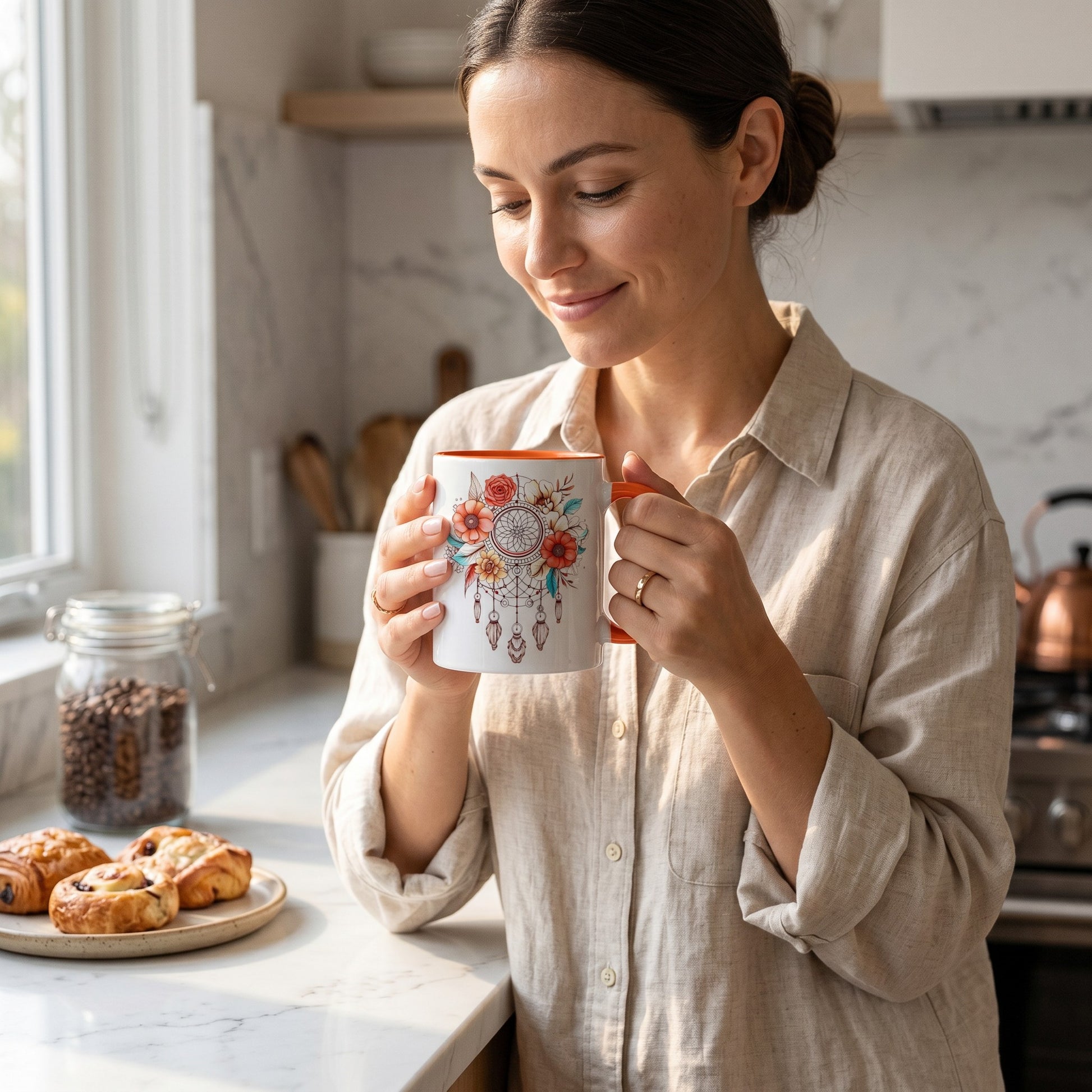 Woman holding an Illustrated Solutions Store ceramic mug with a floral dreamcatcher design in a bright kitchen.