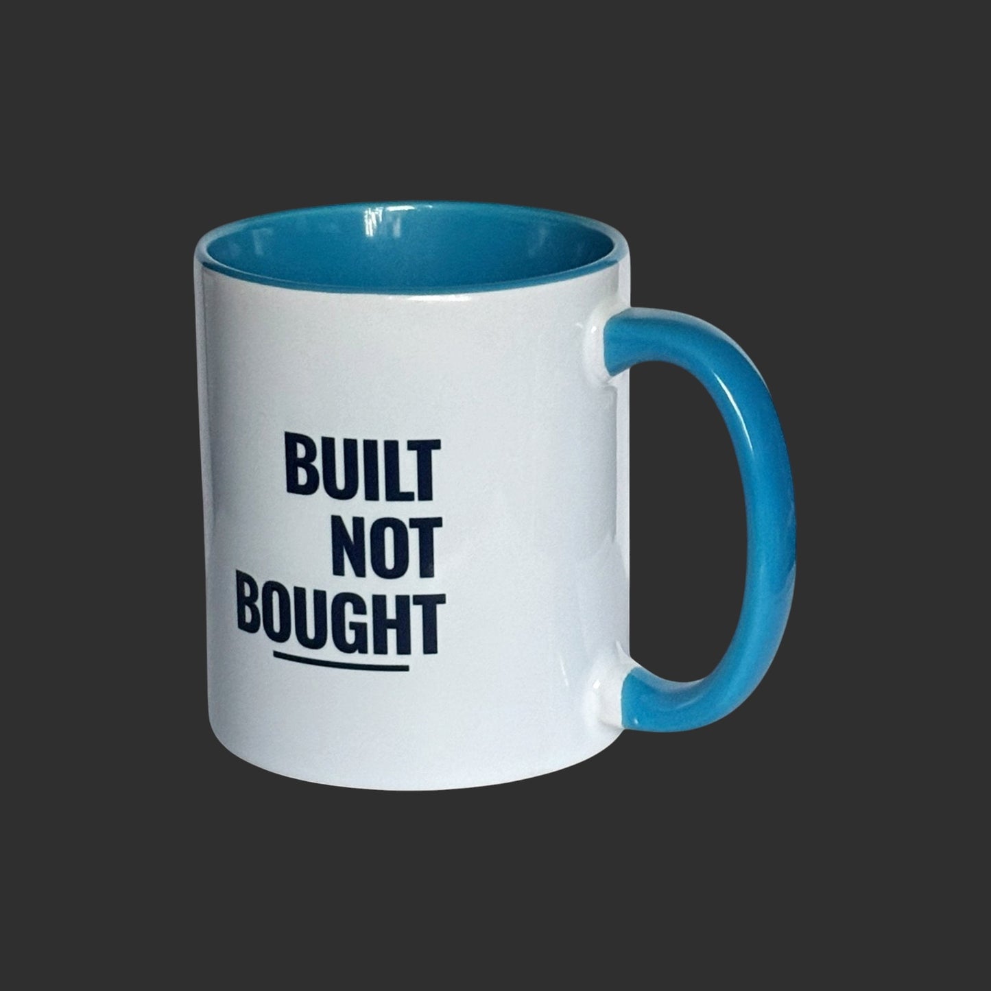 Illustrated Solutions Store white ceramic mug with blue interior and handle, featuring the text "BUILT NOT BOUGHT" in navy blue.