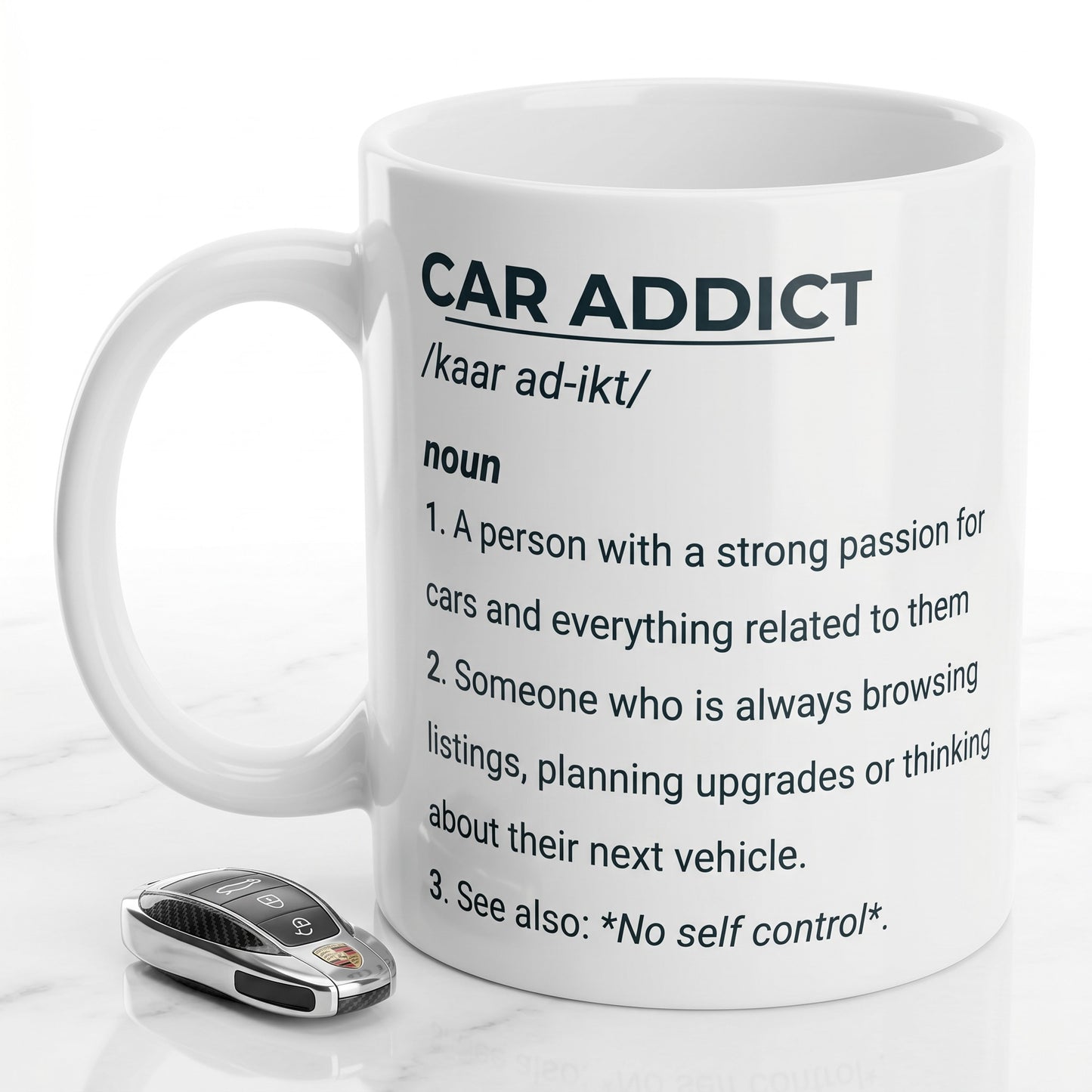 Illustrated Solutions Store white ceramic mug featuring a Car Addict definition print next to a car key fob.
