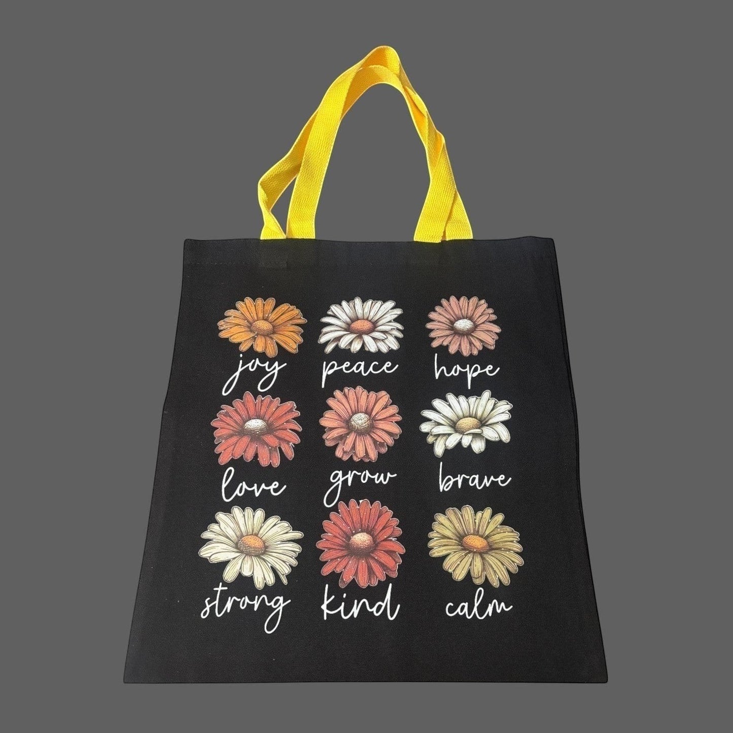 Illustrated Solutions Store black canvas tote bag with yellow handles, featuring a grid of daisy illustrations with positive affirmations like joy, peace, hope, love, grow, brave, strong, kind, and calm.
