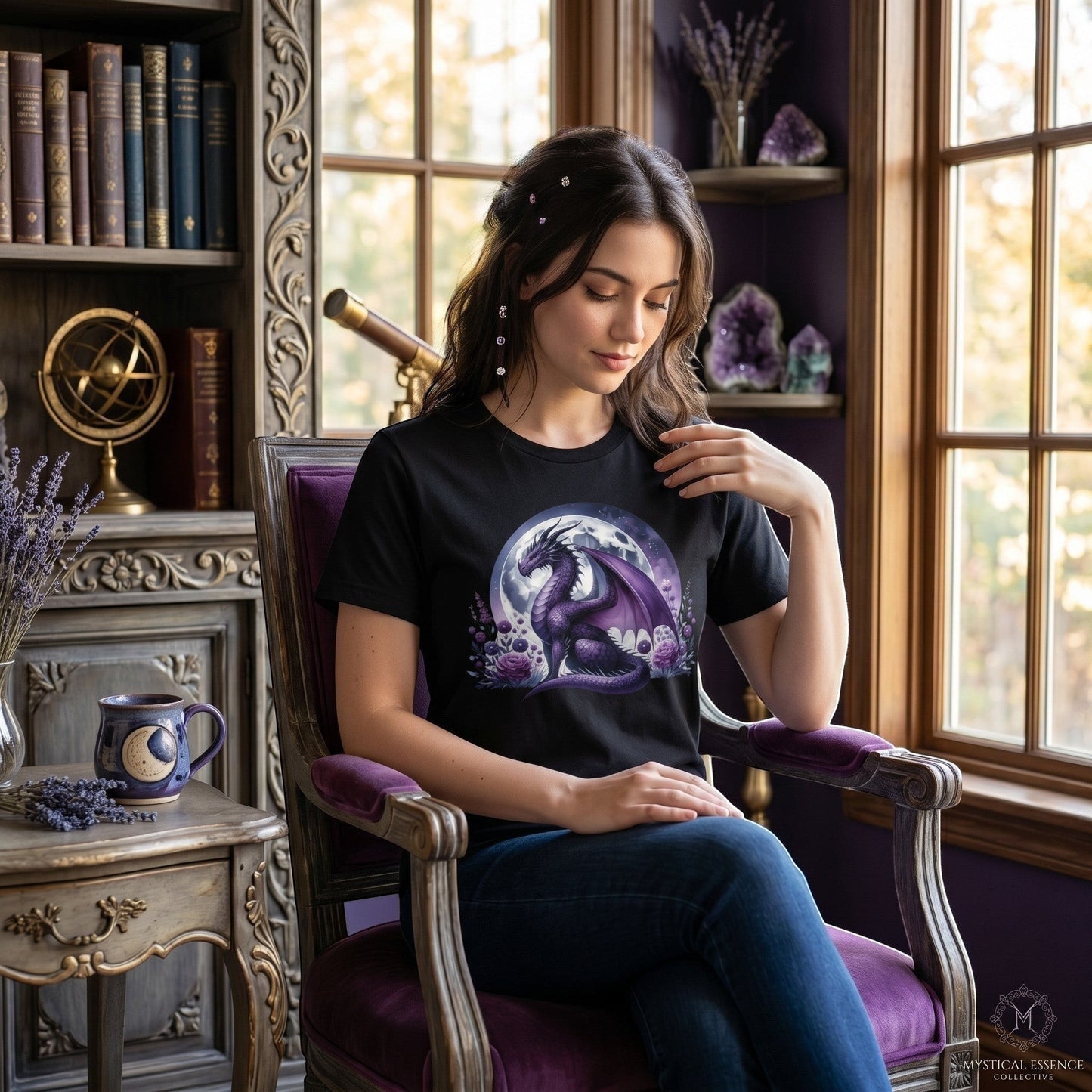 Illustrated Solutions Store black t-shirt with a purple dragon and moon graphic worn by a woman in a cozy library.