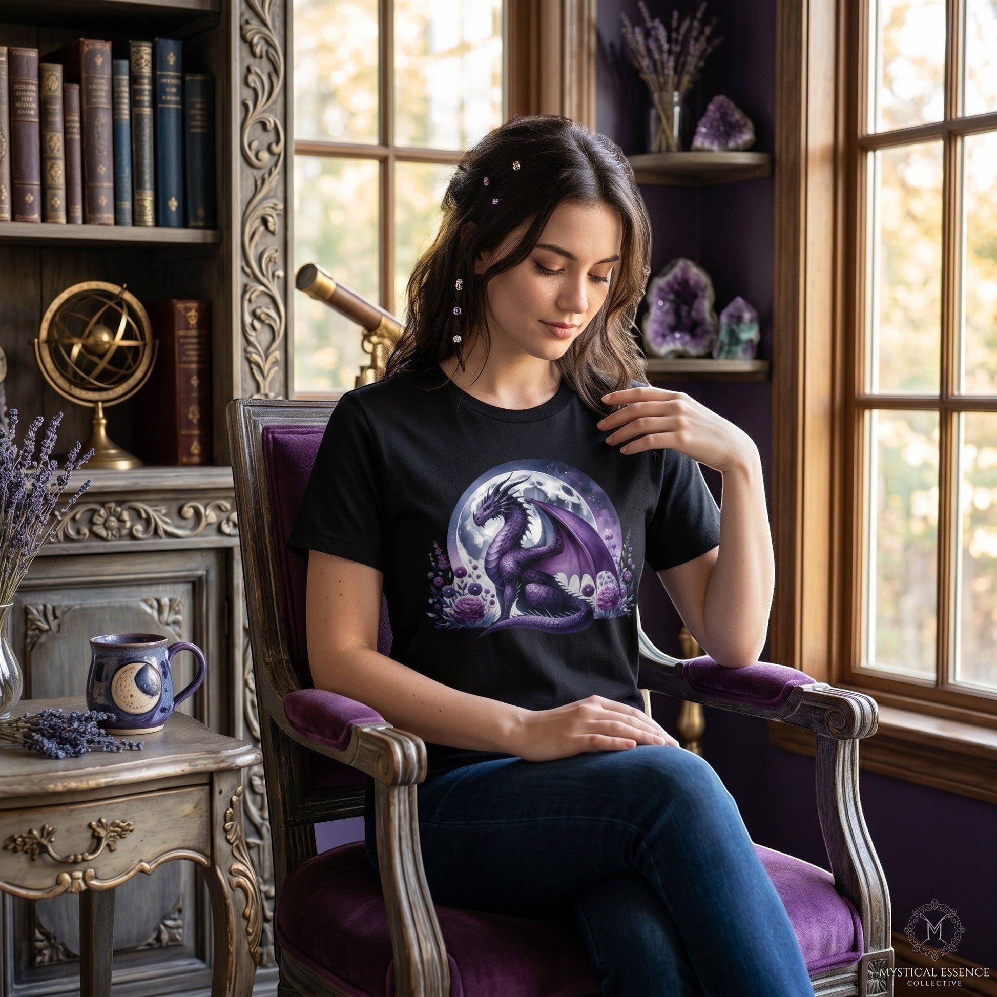 Illustrated Solutions Store black t-shirt with a purple dragon and moon graphic worn by a woman in a cozy library.