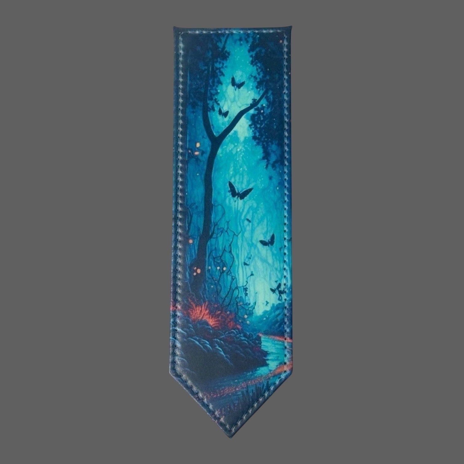 Illustrated Solutions Store leather bookmark with a deep teal enchanted forest scene, featuring butterflies and glowing lights.