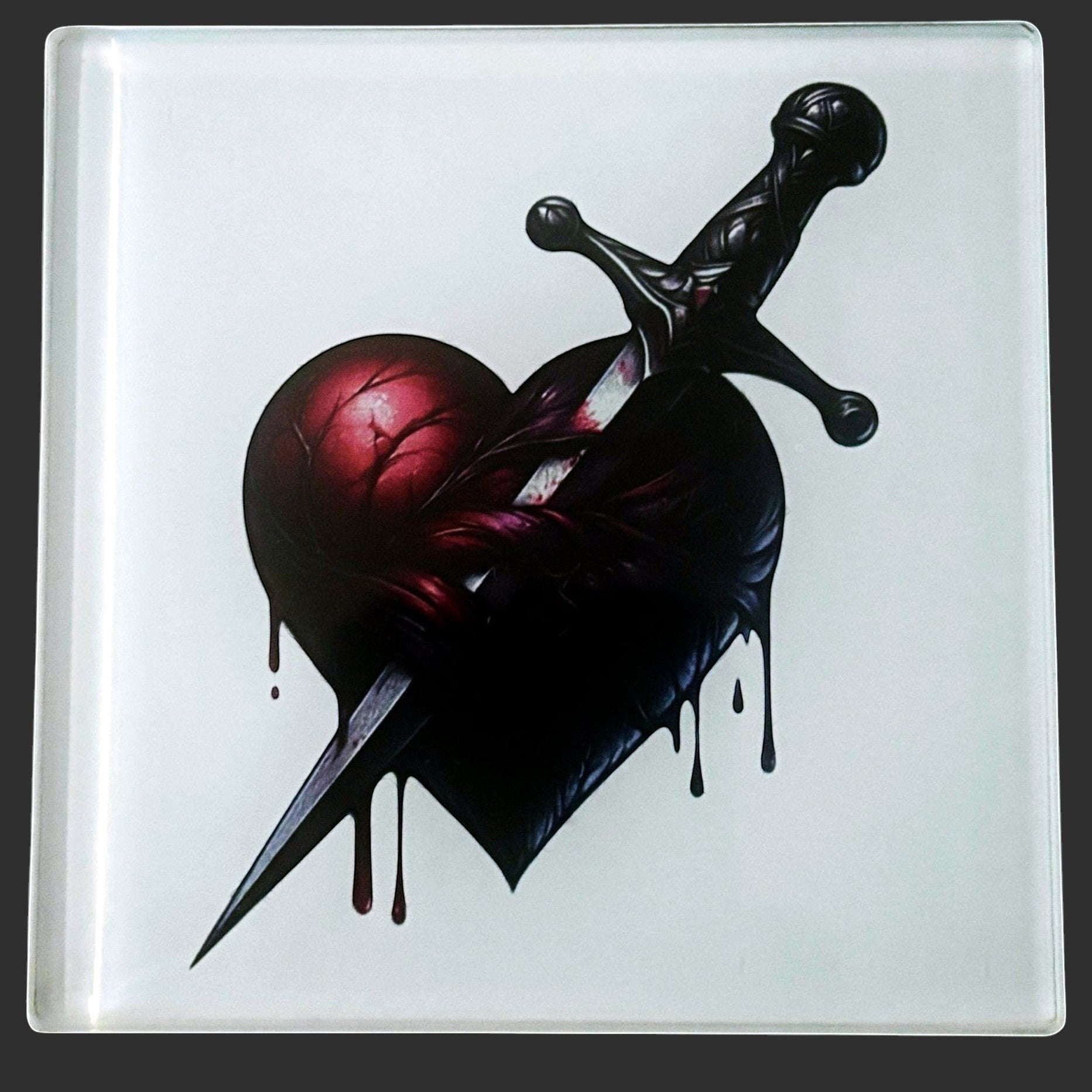 Illustrated Solutions Store gothic heart dagger glass coaster. Features a dark, dripping heart pierced by a dagger. Close-up view.