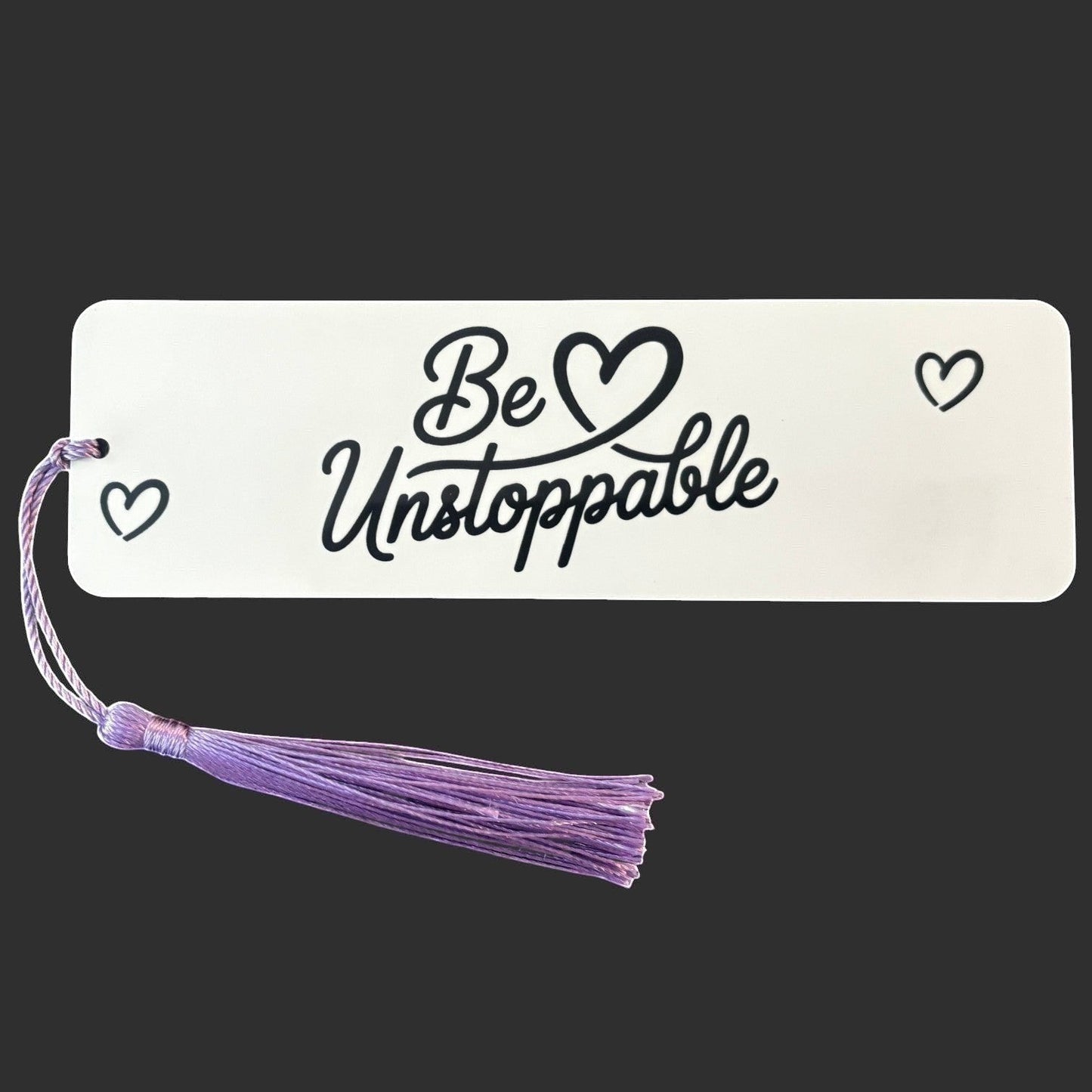 Illustrated Solutions Store metal bookmark with Be Unstoppable text and purple tassel on a white background.