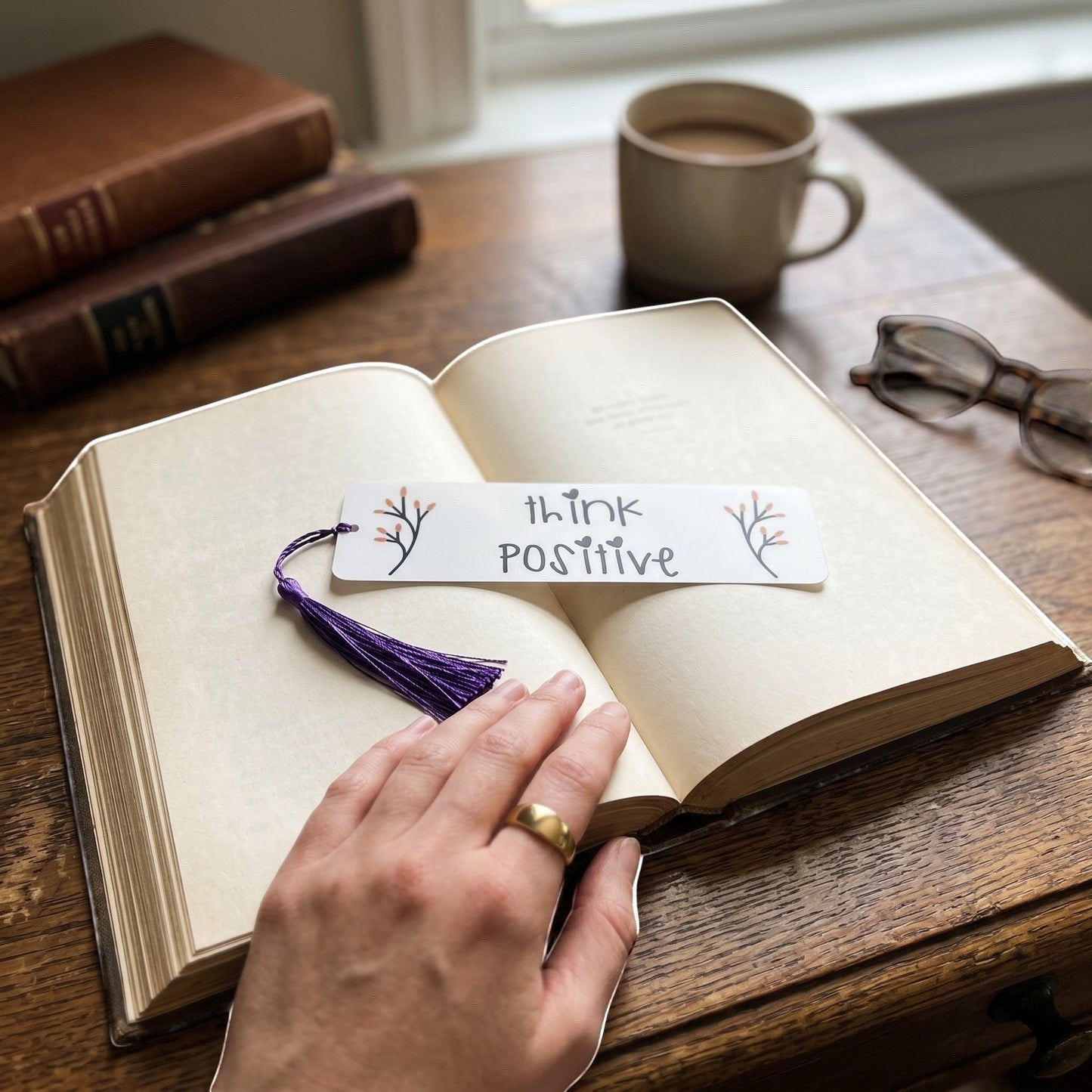 Illustrated Solutions Store aluminium bookmark with Think Positive text and purple tassel resting on an open book.