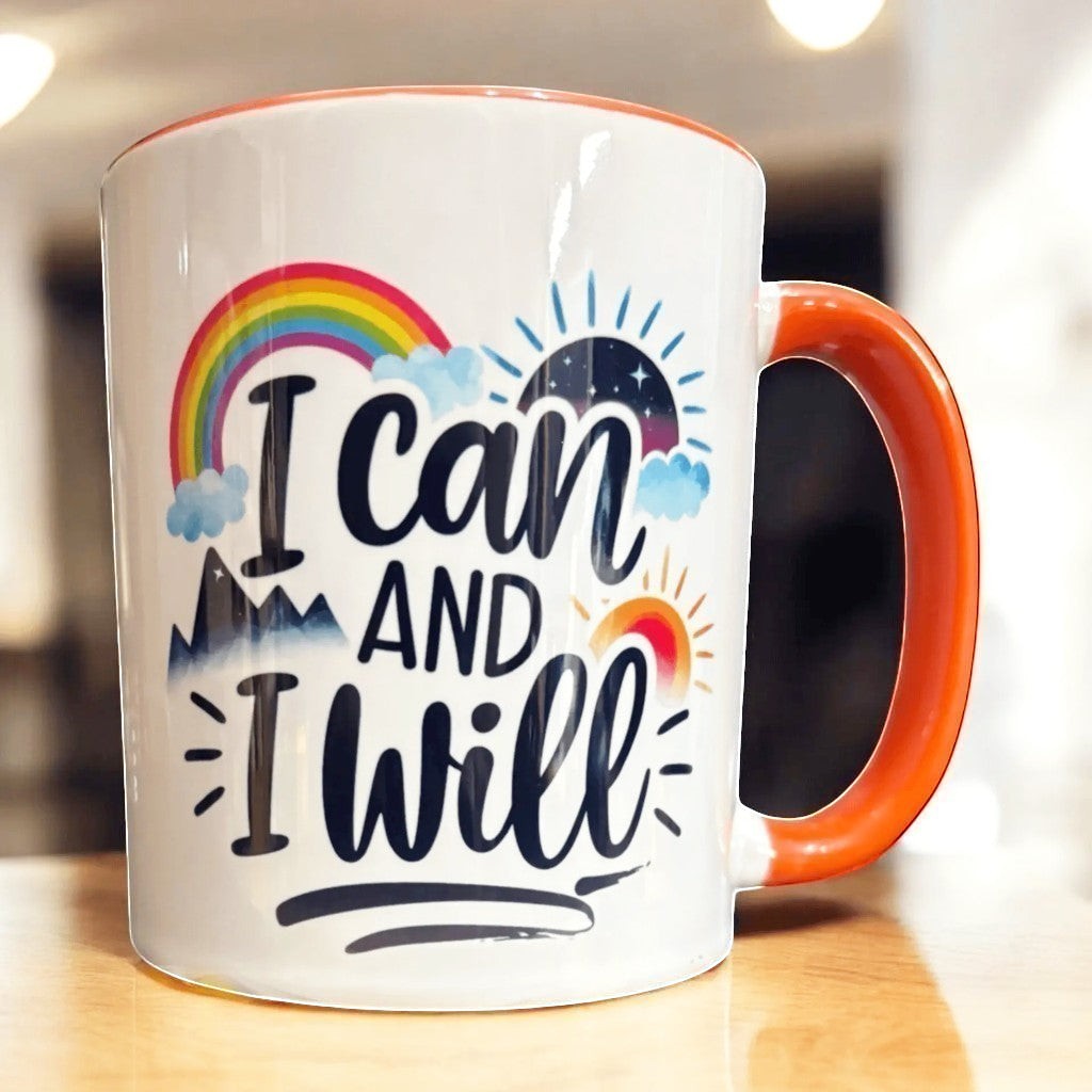 Illustrated Solutions Store white ceramic mug with orange handle, featuring the text "I can AND I will" with a rainbow, mountains, and sun graphics.