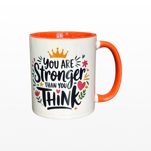 Illustrated Solutions Store white ceramic mug with orange handle and interior, featuring the quote "You are stronger than you think" in black lettering with floral accents.