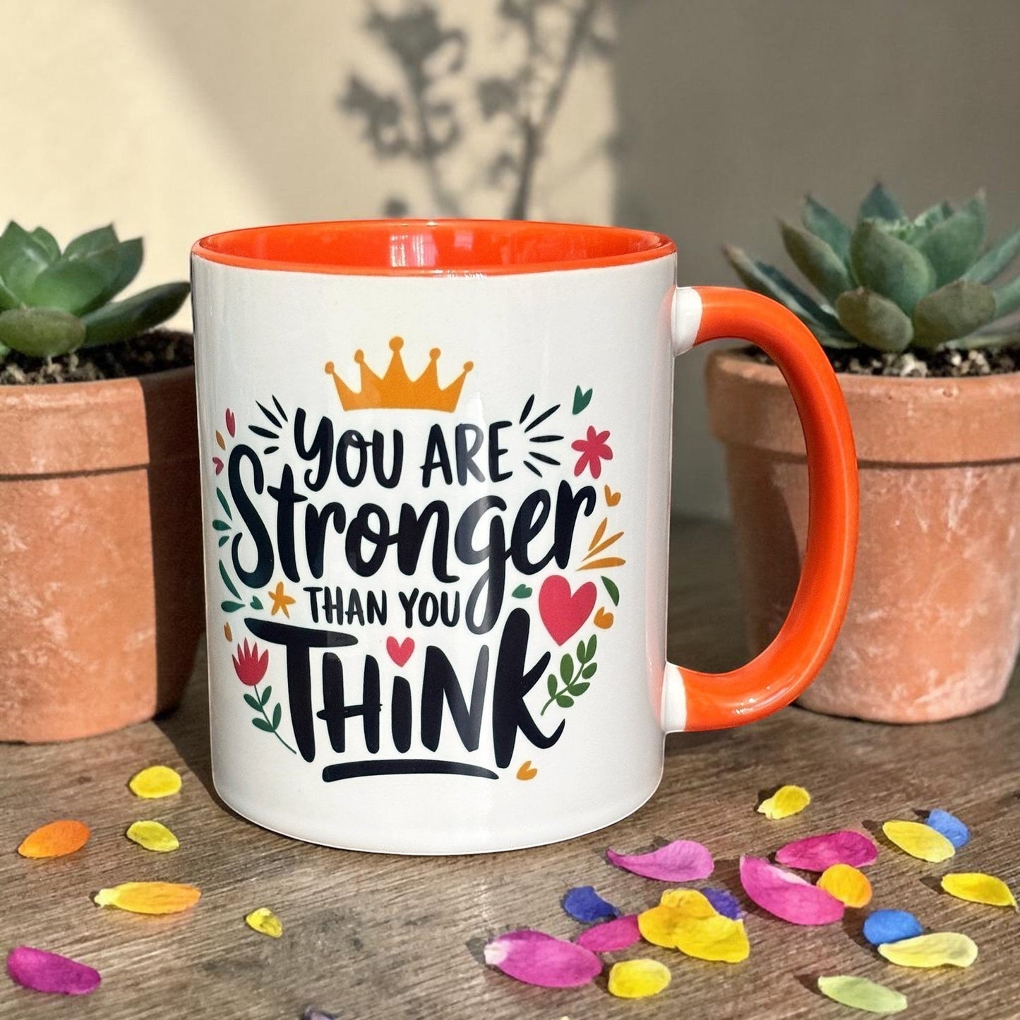 Illustrated Solutions Store motivational mug with orange handle and interior, featuring the text "You are stronger than you think" with floral accents and a crown.