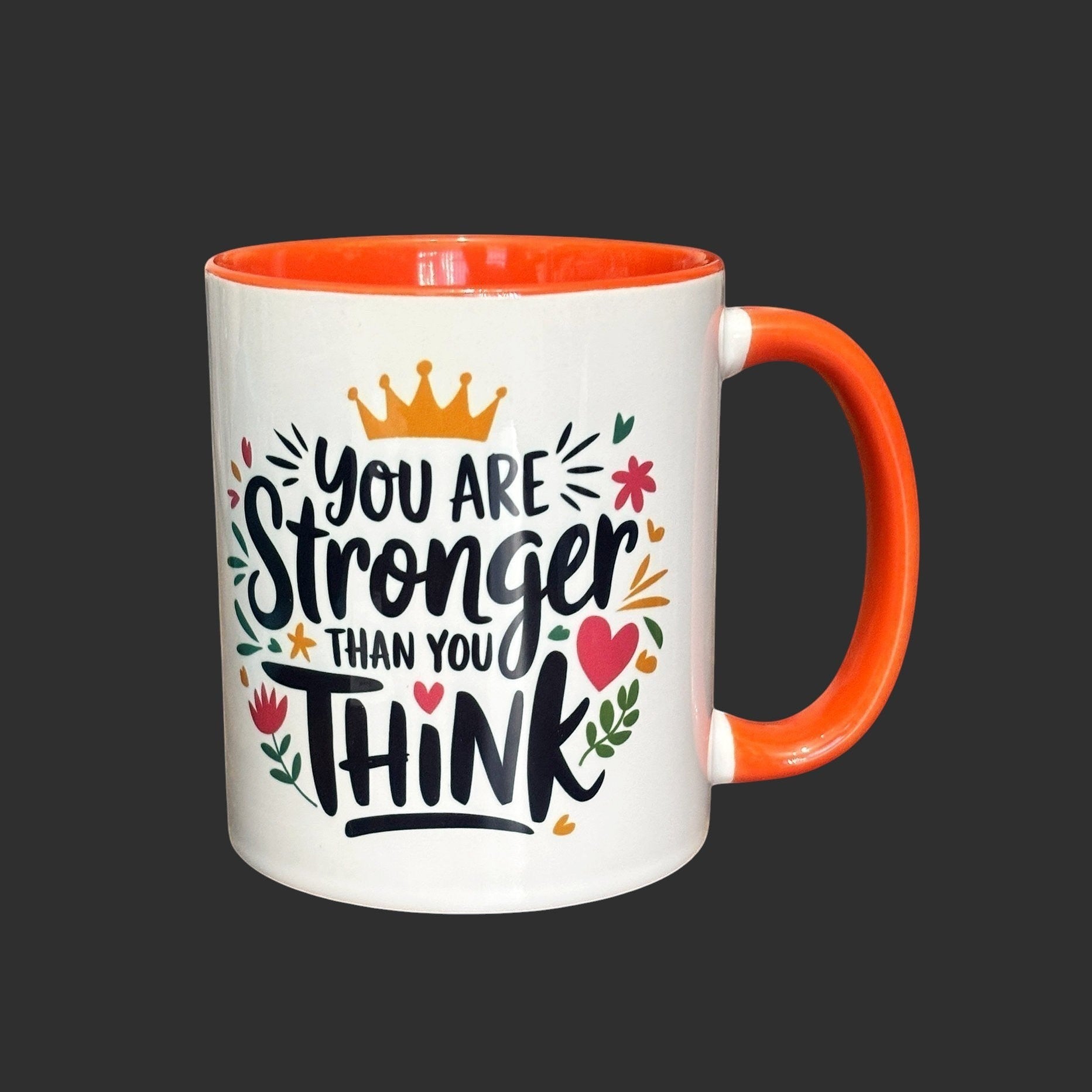 Illustrated Solutions Store white ceramic mug with orange handle and interior, featuring the text "You are stronger than you think" with floral and crown graphics.