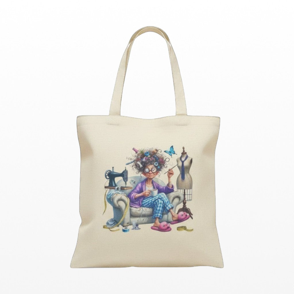 Illustrated Solutions Store cream canvas tote bag with a humorous sewing design of a woman with wild hair, sewing machine, and mannequin.