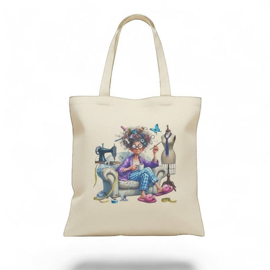 Illustrated Solutions Store cream canvas tote bag with a humorous sewing design of a woman with wild hair, sewing machine, and mannequin.