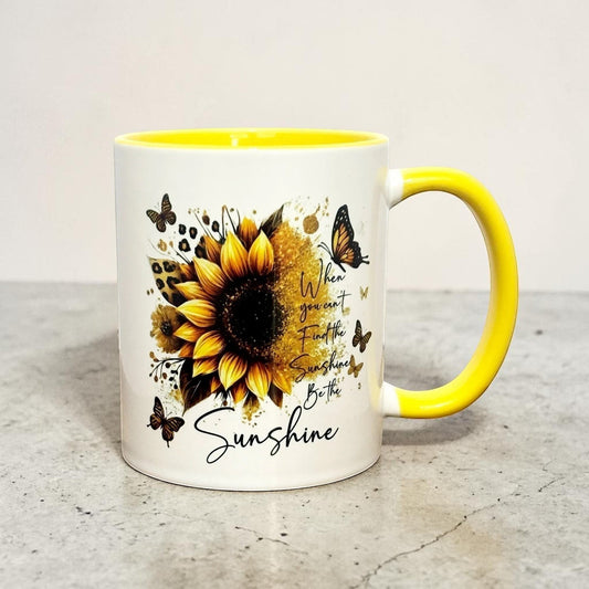Illustrated Solutions Store white ceramic mug with yellow handle and interior, featuring a sunflower, butterflies, and the text "When you can't find the sunshine, be the sunshine."