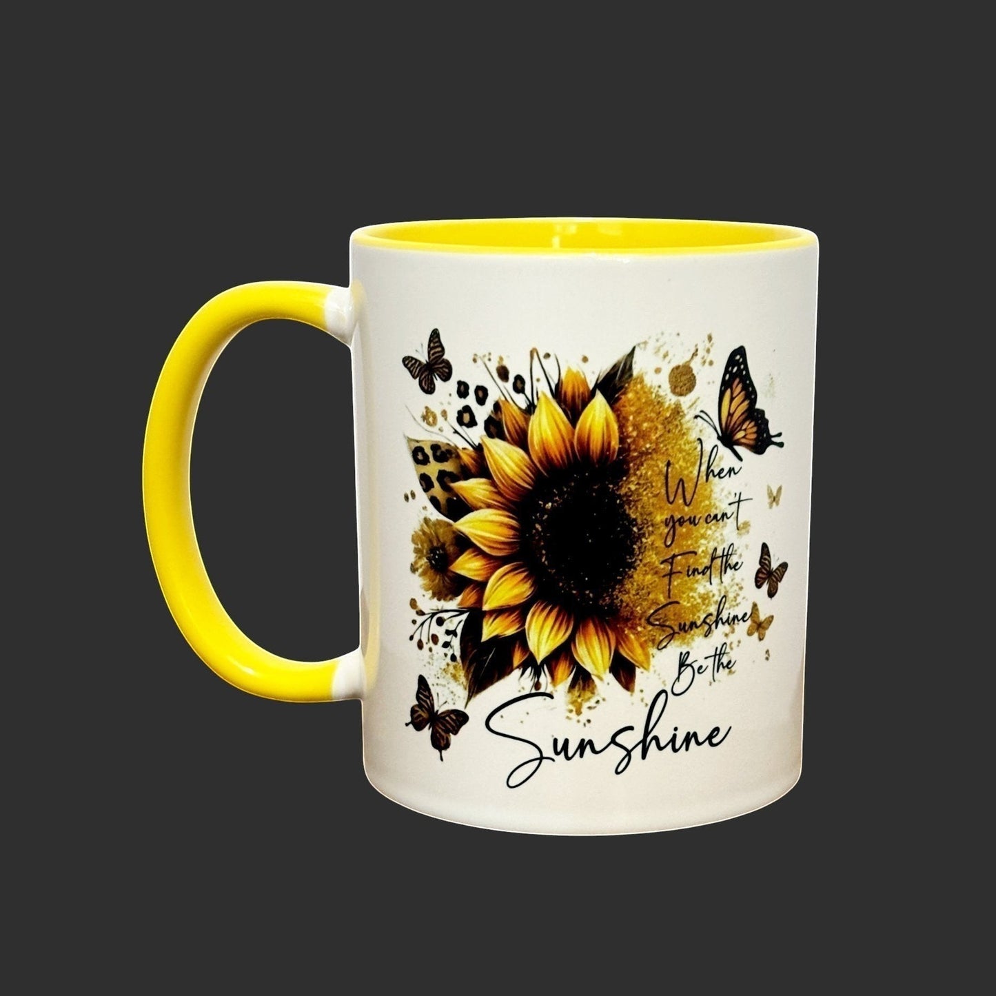 Illustrated Solutions Store white ceramic mug with yellow handle and interior, featuring a sunflower, butterflies, and the text "When you can't find the sunshine, be the sunshine."