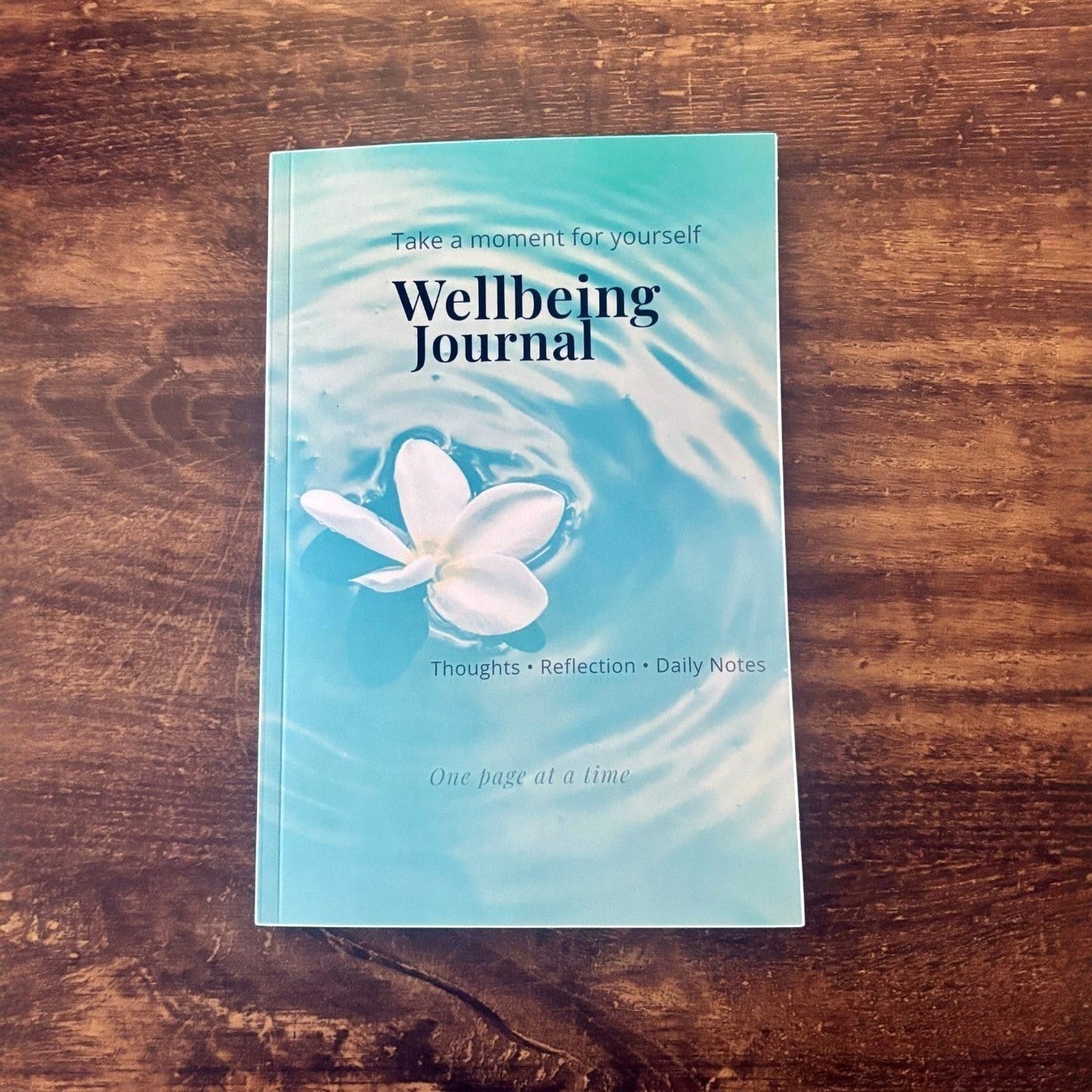 Illustrated Solutions Store Wellbeing Journal with a white flower floating on rippling blue water, for mindfulness and reflection.