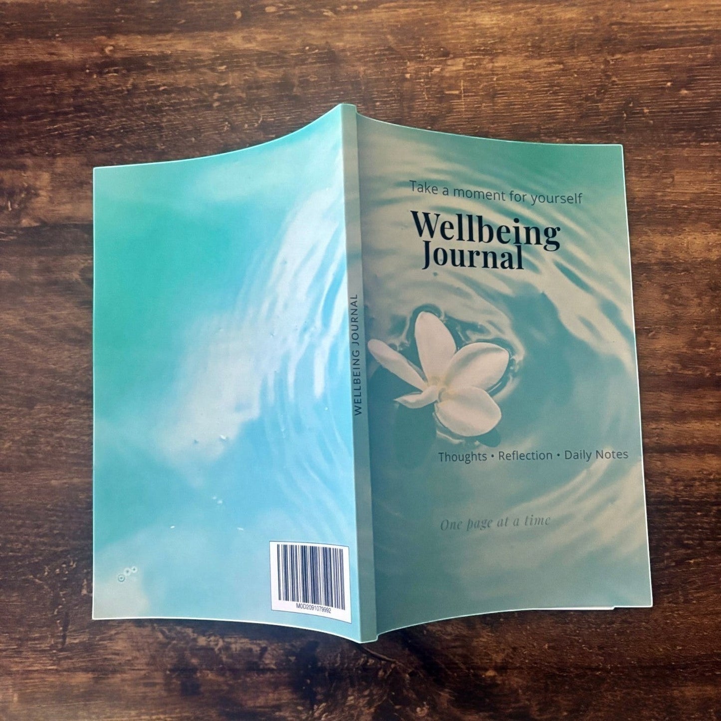 Illustrated Solutions Store wellbeing journal with a calming water design and a white flower floating on the surface. Features 'Thoughts, Reflection, Daily Notes'.