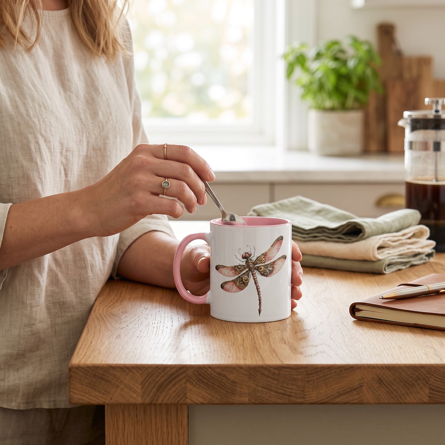 Pink ceramic mug with steampunk dragonfly art, pink handle, and interior, held in a kitchen.