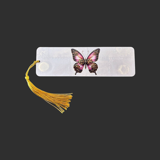 Horizontal view of an aluminium bookmark featuring an original pink steampunk butterfly illustration with bronze clockwork detailing and a gold tassel.