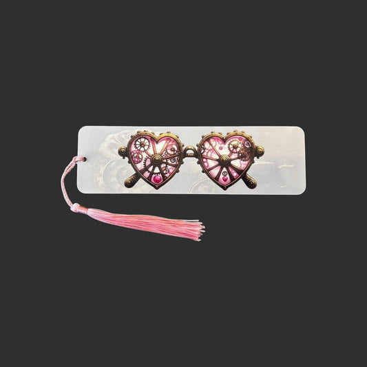 Horizontal view of an aluminium bookmark featuring original pink steampunk heart-shaped glasses with intricate bronze clockwork detailing and a matching pink tassel.