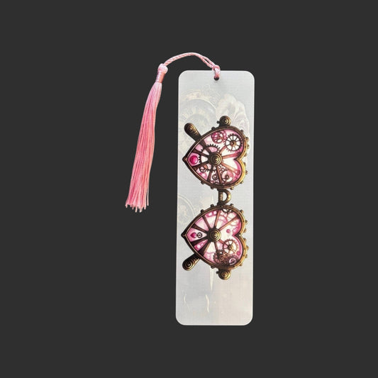 Vertical view of an aluminium bookmark featuring original pink steampunk heart-shaped glasses with intricate bronze clockwork detailing and a matching pink tassel.