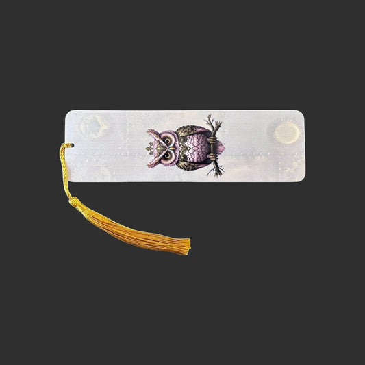 Horizontal view of an aluminium bookmark featuring an original pink steampunk owl illustration with intricate clockwork detailing and a gold tassel.