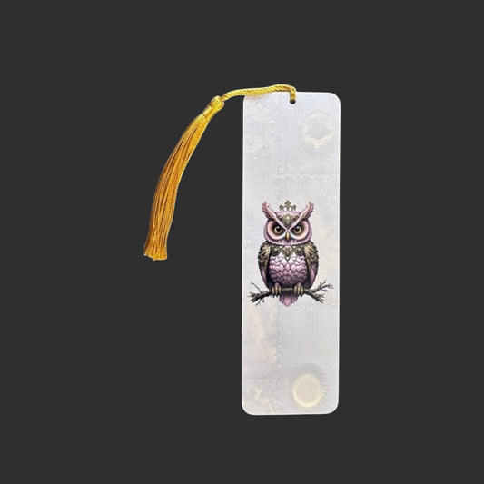 Vertical view of an aluminium bookmark featuring an original pink steampunk owl illustration with intricate clockwork detailing and a gold tassel.