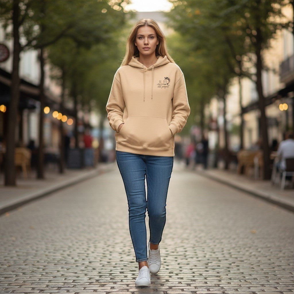 Woman walking on a street wearing a beige hoodie and blue jeans.